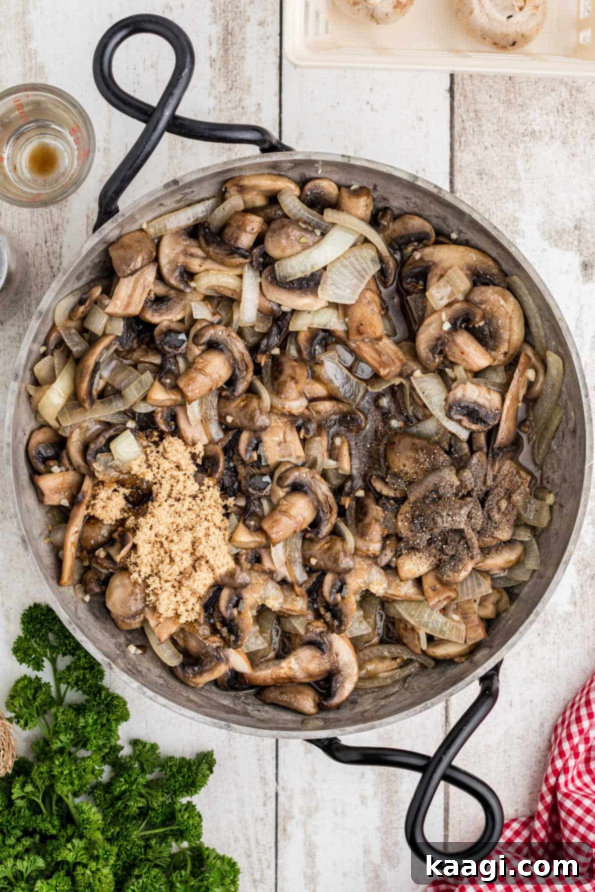 An overhead shot showing the various ingredients, including brown sugar, Worcestershire sauce, and black pepper, being added to the sautéing mushrooms and onions in a skillet.