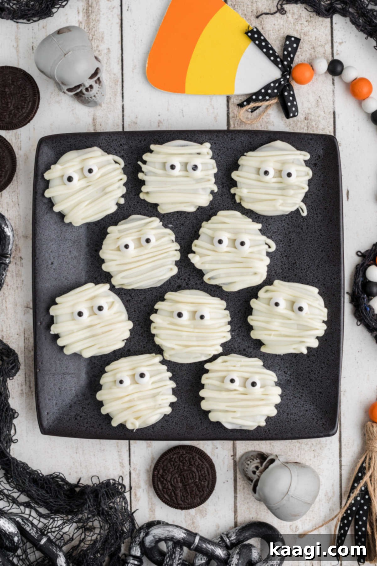 Mummy Oreos on a square black plate from overhead, with halloween decorations all around, ready for a festive display.