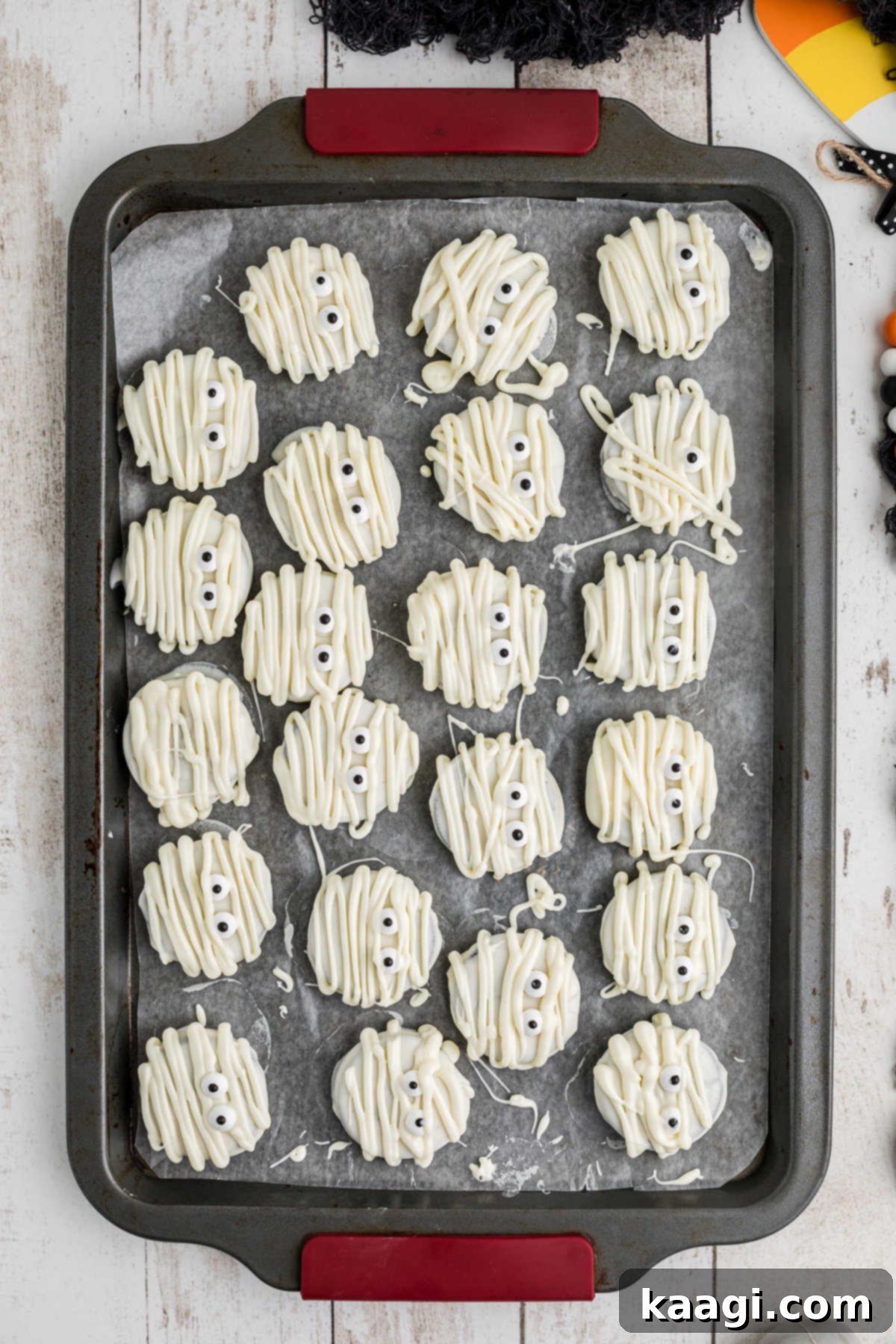 A baking sheet full of partially coated mummy oreos, ready for eyes and bandages.