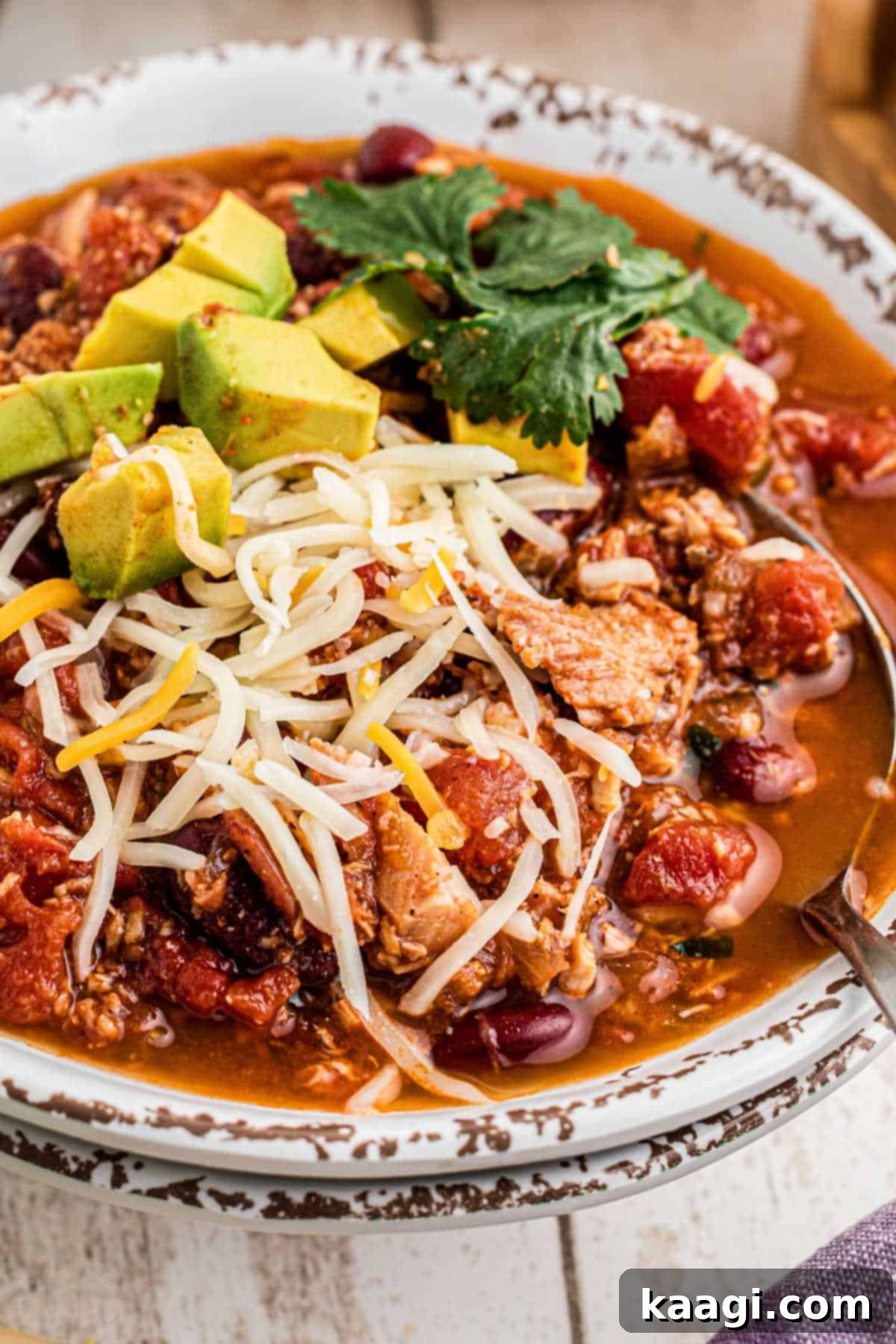 Rich and Hearty Dutch Oven Turkey Chili 2 Close up of a bowl of Dutch oven turkey chili with cheese and avocado sprinkled on top.