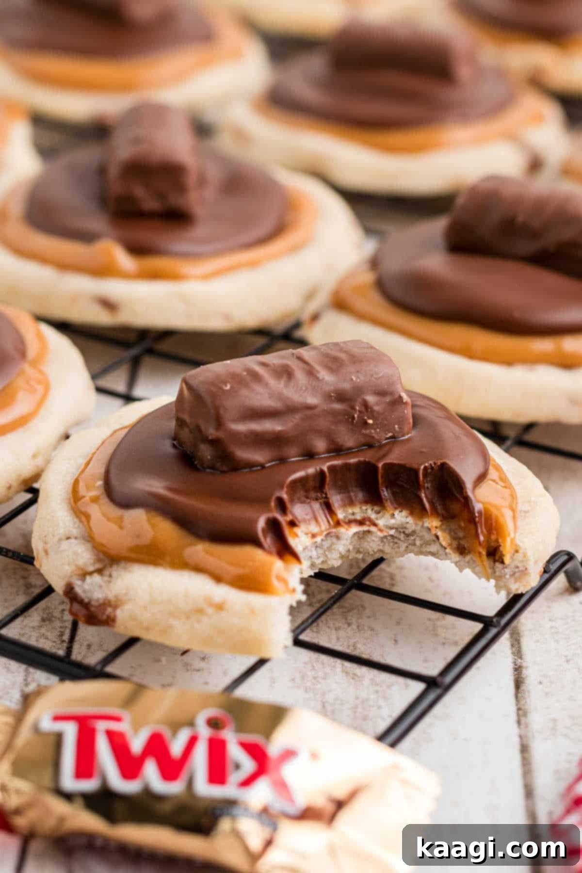 Portrait image of a cooling rack full of crumbl twix cookies., one with a bite taken out.