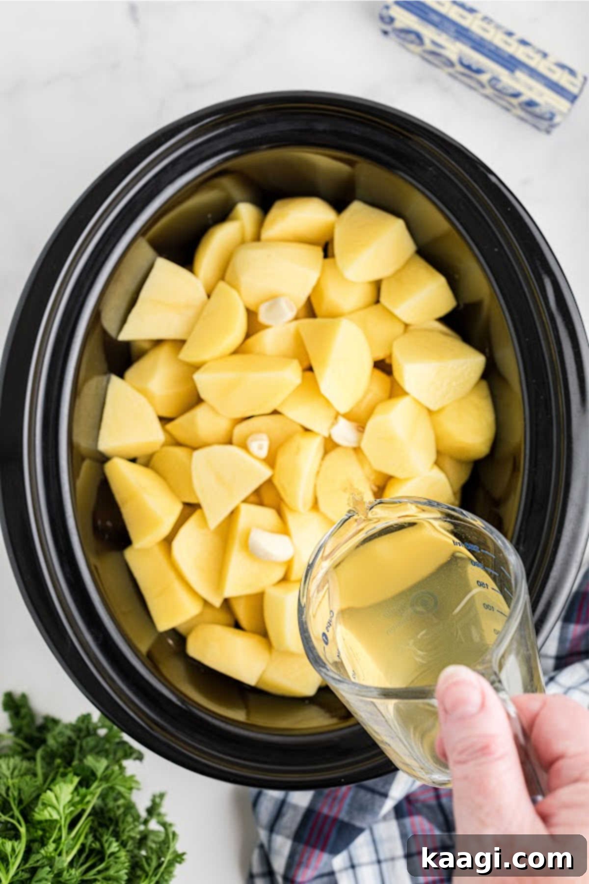 Savory Slow Cooker Mashed Potatoes 6 Broth being added to a slow cooker full of potatoes.