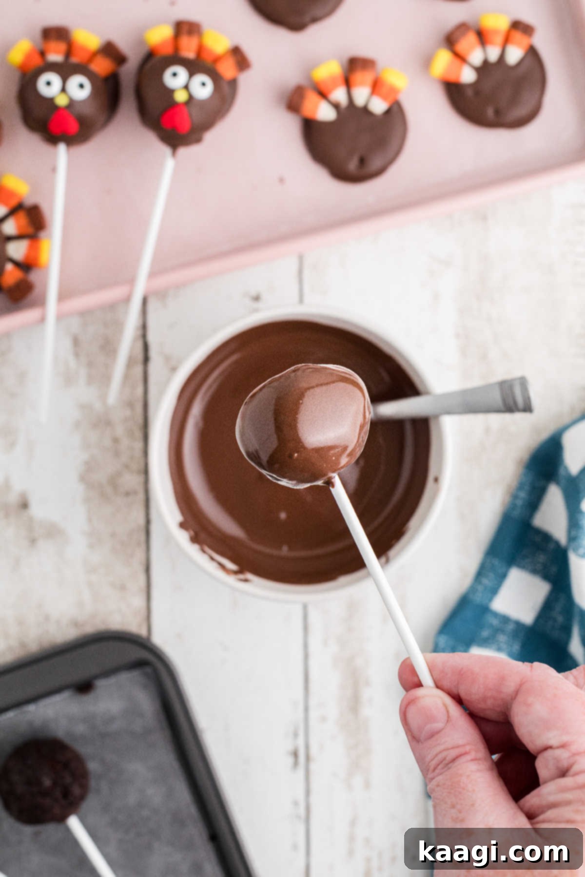 Festive Thanksgiving Cake Pops 7 A cake pop on a stick being carefully dipped into a bowl of melted chocolate almond bark.