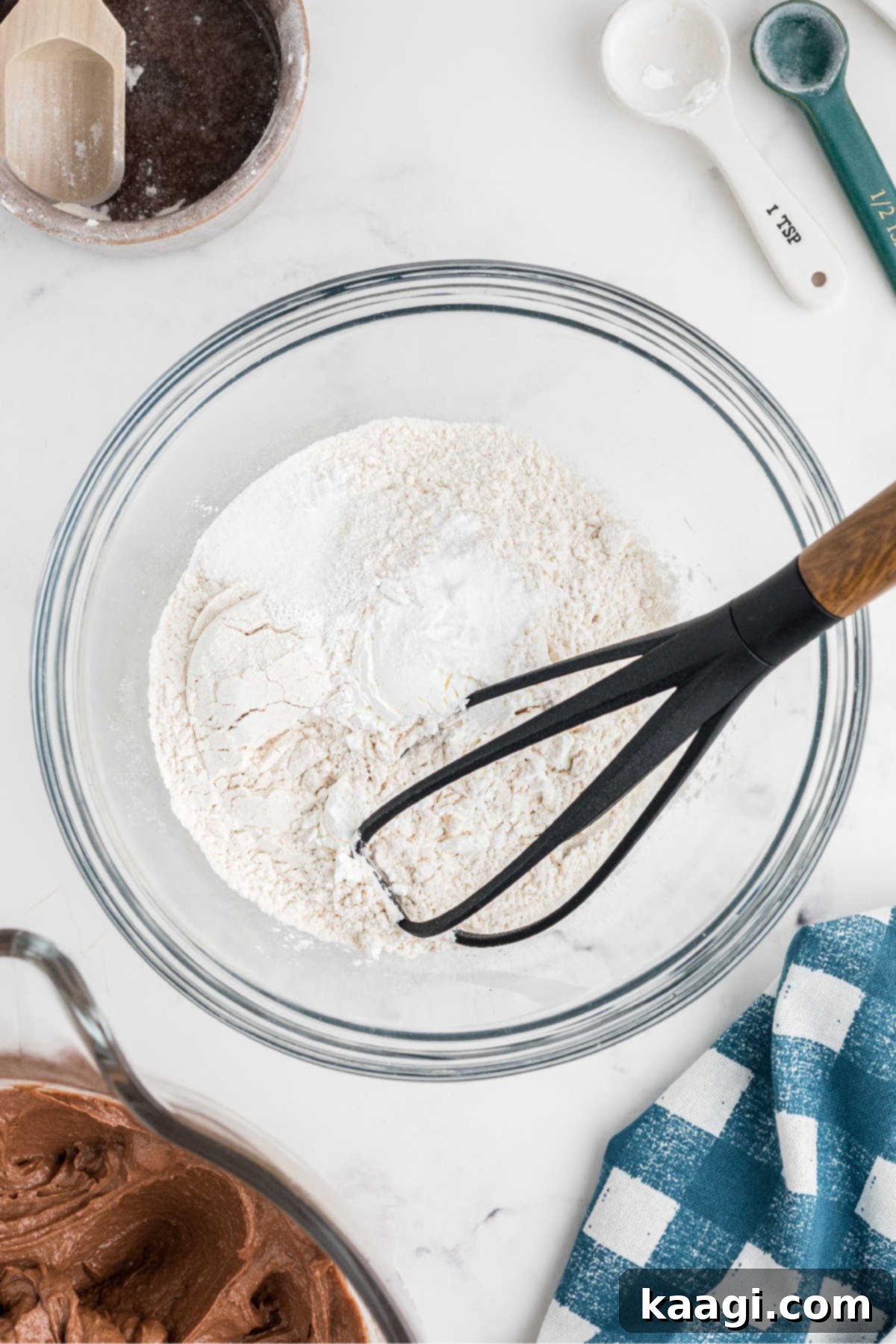 A separate mixing bowl containing flour, cornstarch, baking powder, baking soda, and salt, with a whisk.