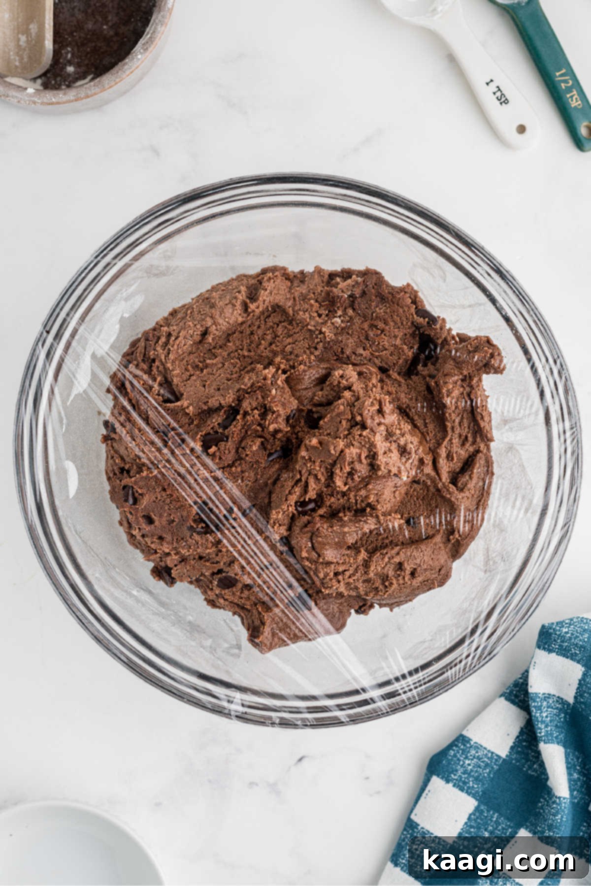 Cookie dough in a mixing bowl covered with plastic wrap, ready for chilling in the refrigerator.