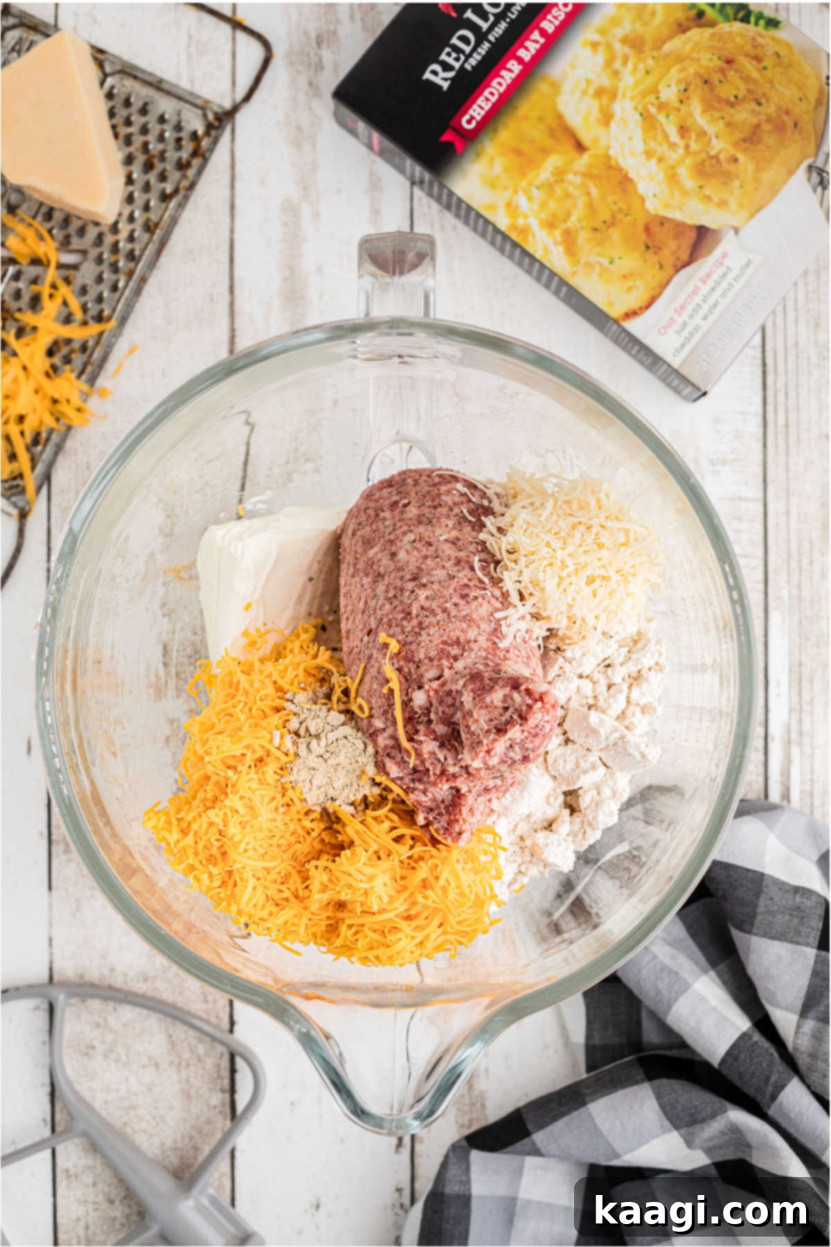 Cheddar Bay Sausage Bites 4 A mixing bowl filled with biscuit mix, raw sausage meat, and shredded cheese, ready to be combined.