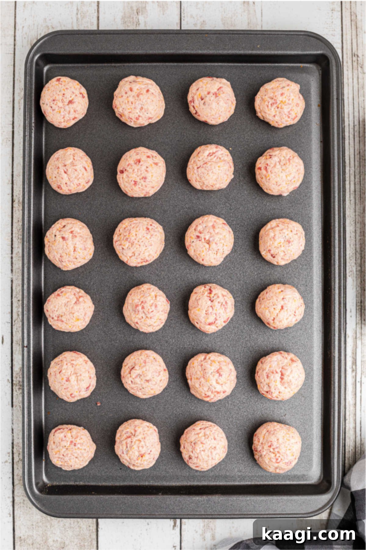 Cheddar Bay Sausage Bites 5 Sausage balls perfectly lined up on a baking sheet, ready for the oven.