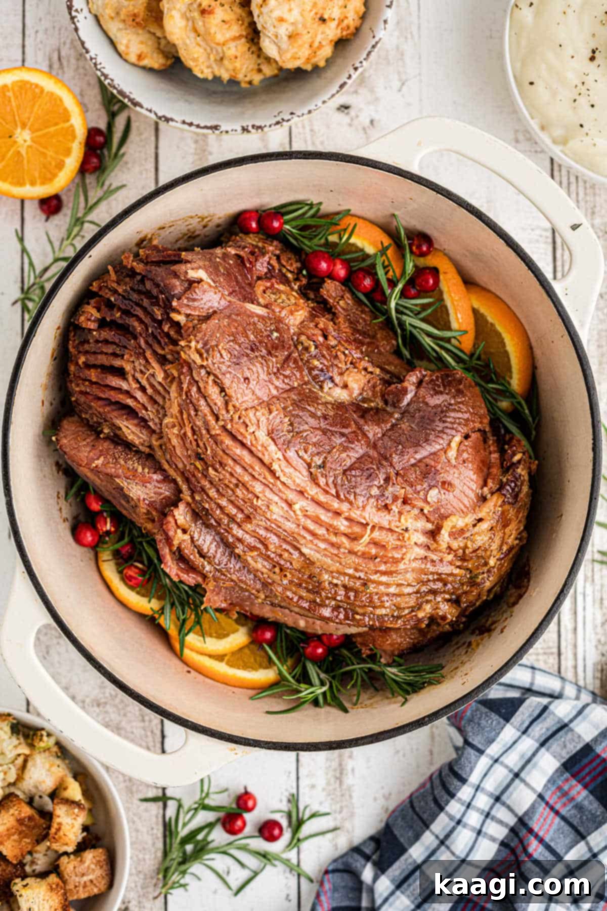 Overhead portrait image of a Dutch Oven Ham with Orange slices on the side, garnished with fresh rosemary.