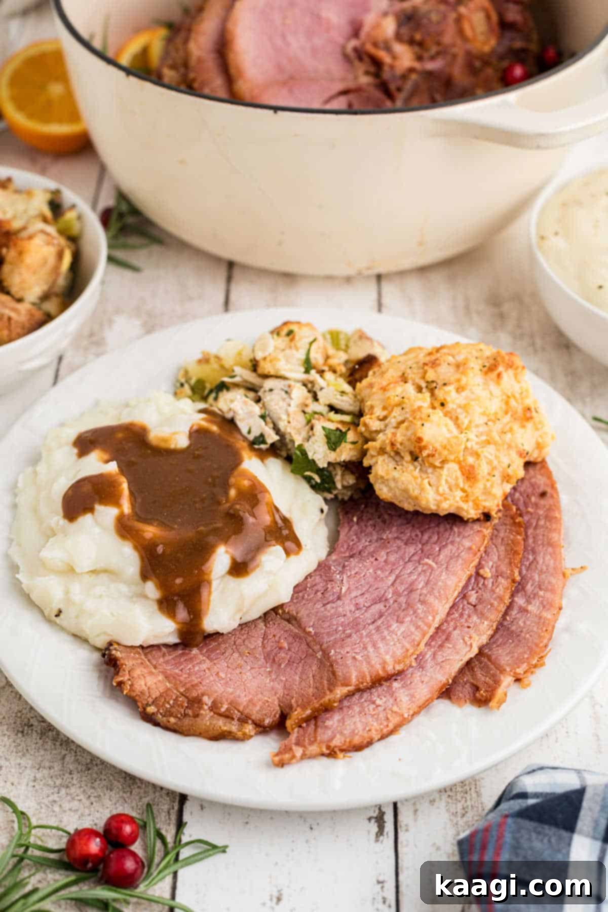 A dished up plate of Dutch Oven Ham with creamy mashed potatoes, savory stuffing, and a slice of bread, ready for a holiday meal.