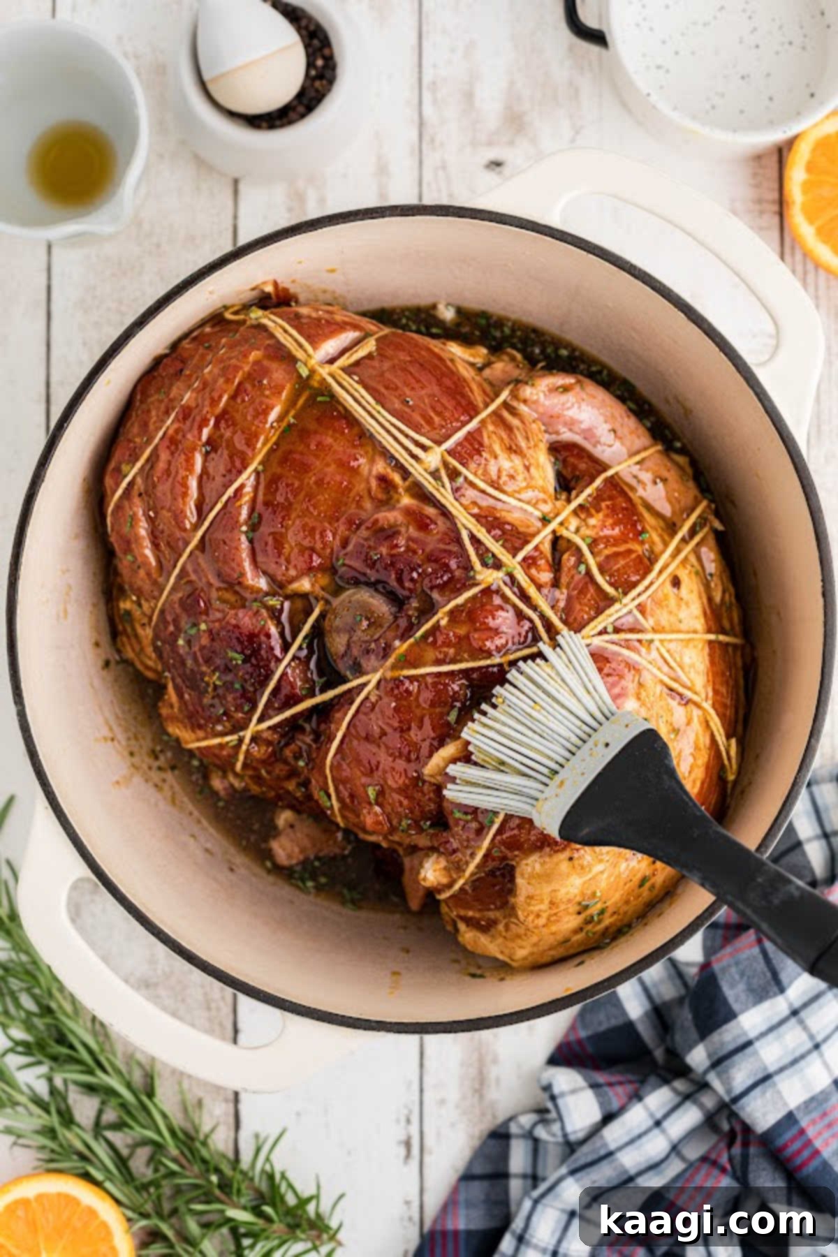 A trussed ham, being brushed generously with a glaze inside a large Dutch oven.