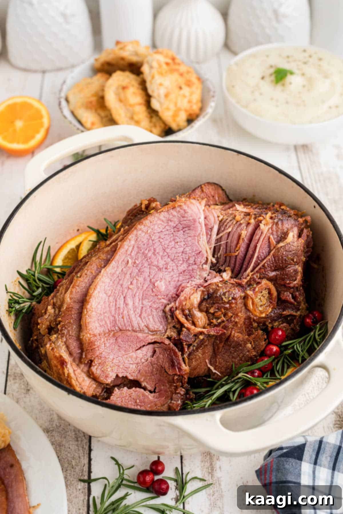 Side angle of a beautifully cooked Dutch Oven Ham garnished with fresh rosemary and orange slices.