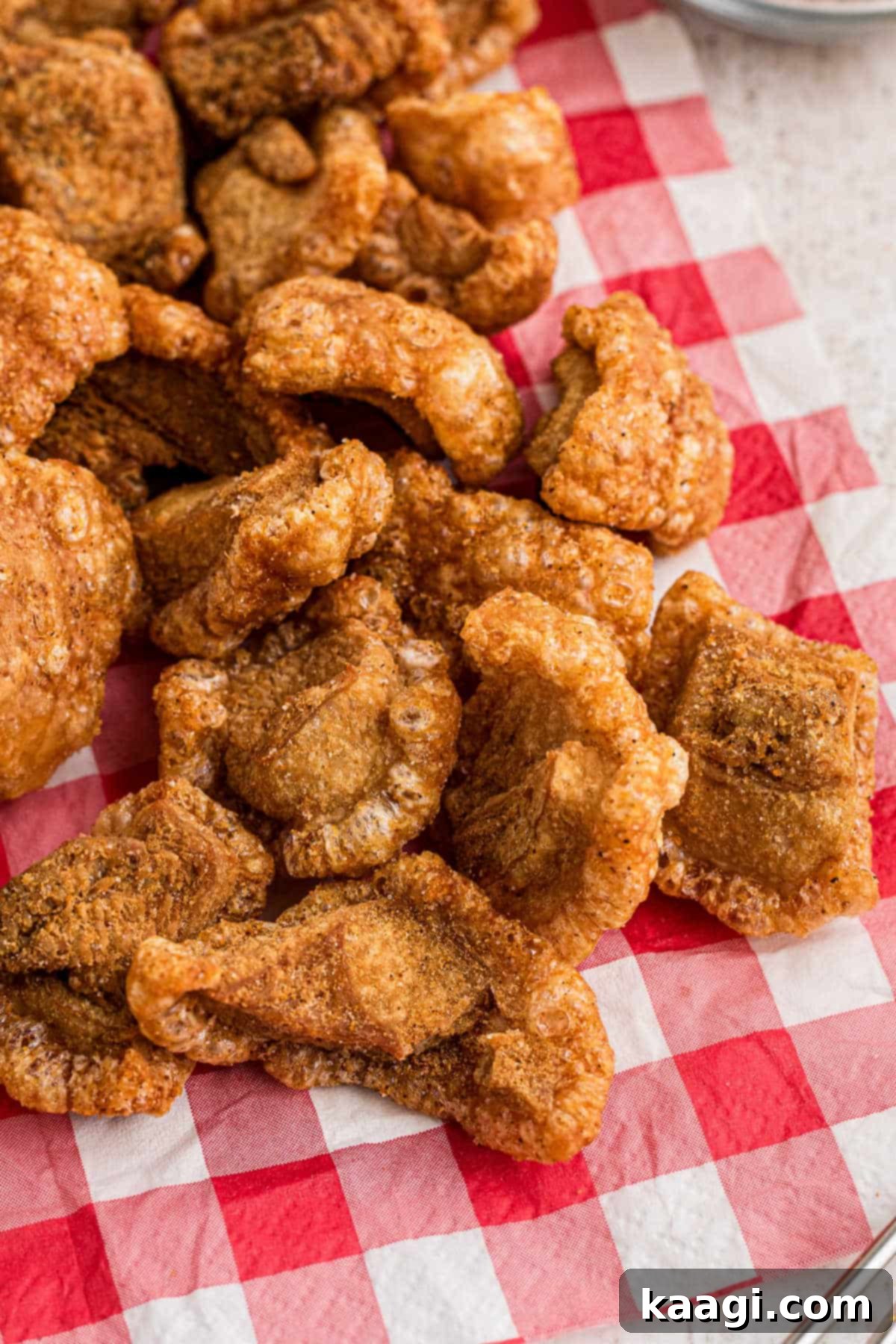 A generous pile of golden-brown, crispy pork cracklins resting on a vibrant red and white checkered napkin.