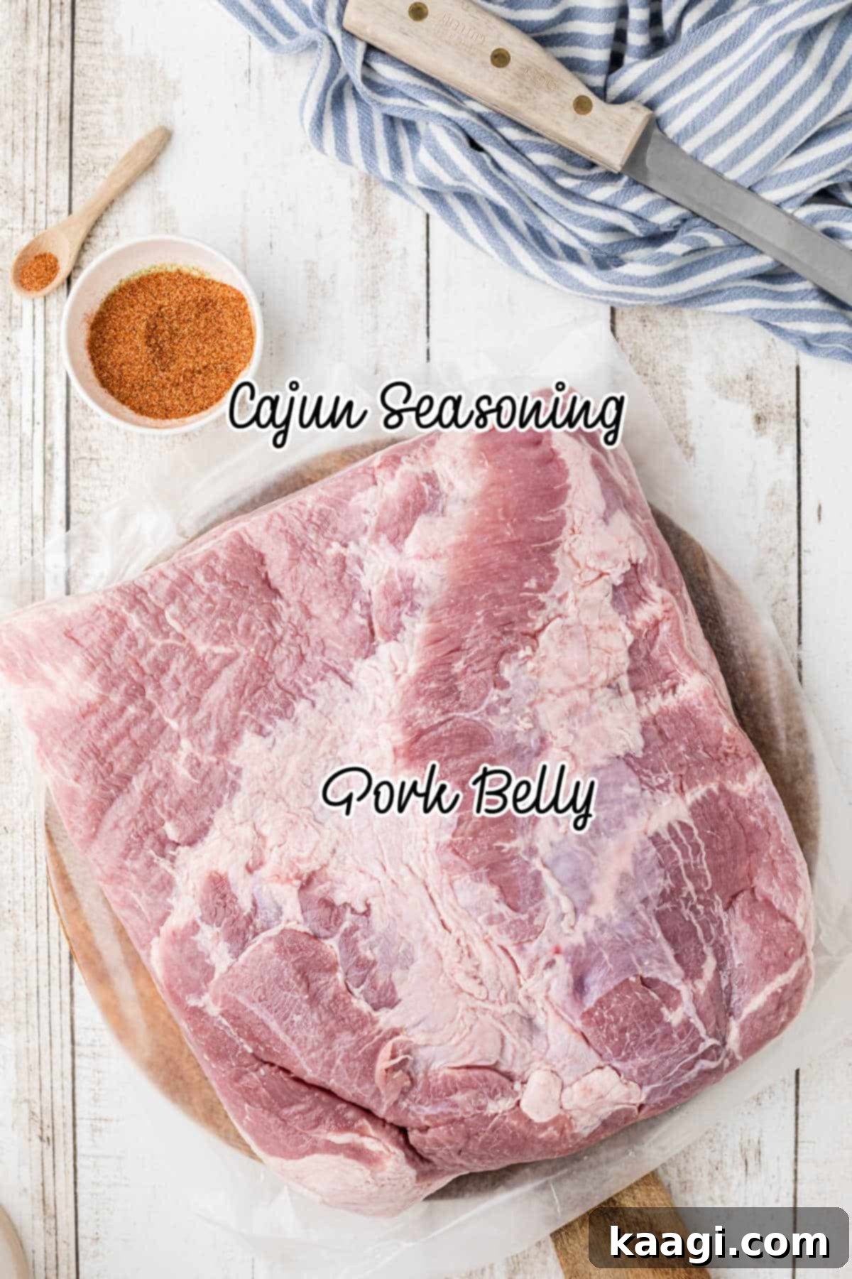 A selection of fresh ingredients laid out, including a large slab of pork belly, a bowl of Cajun seasoning, and a bottle of vegetable oil, ready for making homemade pork cracklins.