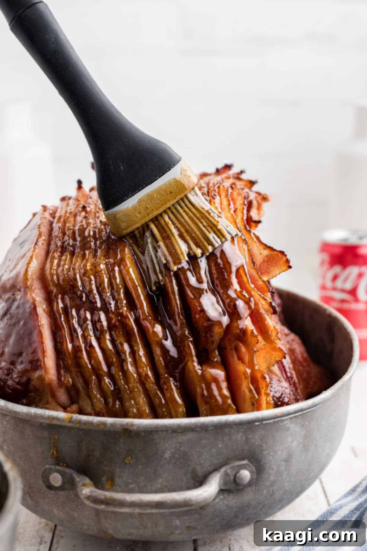 Close up of a basting brush, brushing on a southern coca-cola glaze on a ham, ensuring every crevice is covered.