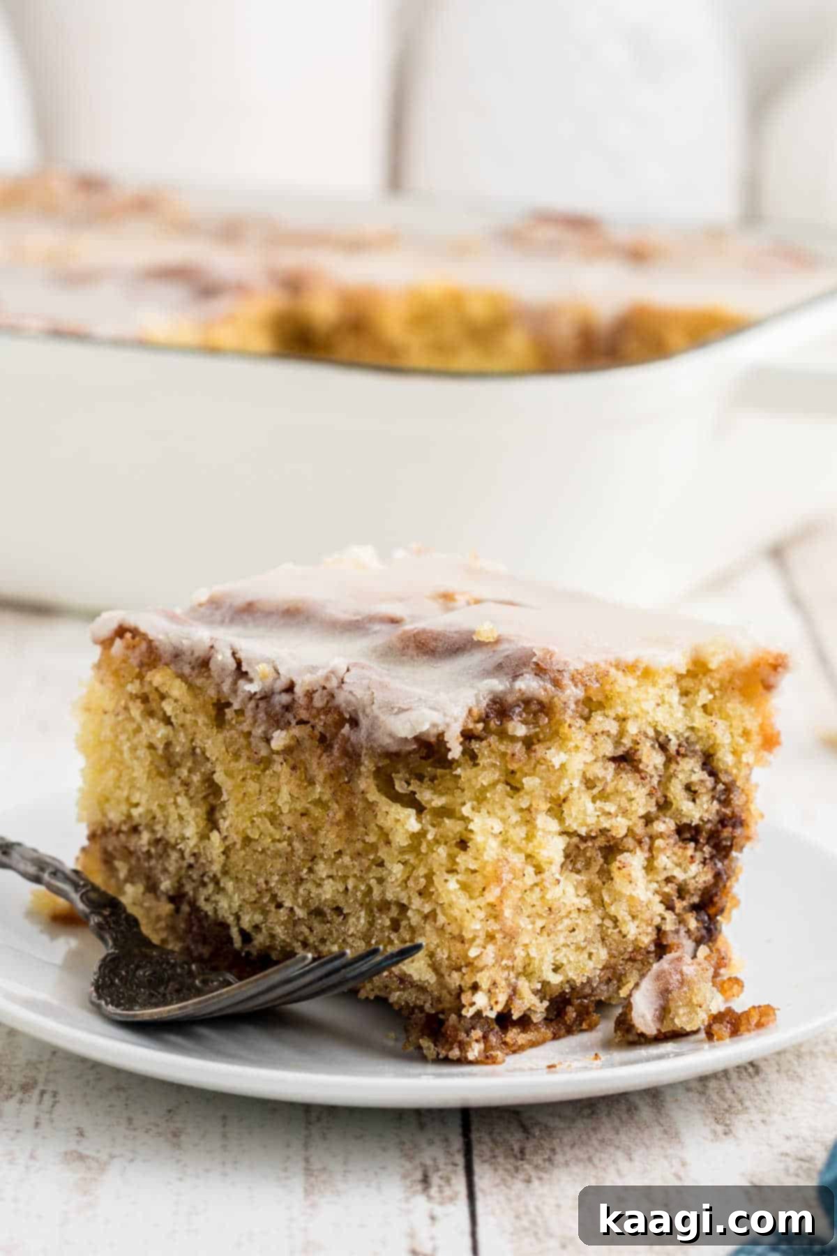 A perfectly sliced piece of homemade honey bun cake, showcasing its gooey cinnamon swirl and sweet glaze, with a fork resting beside it.