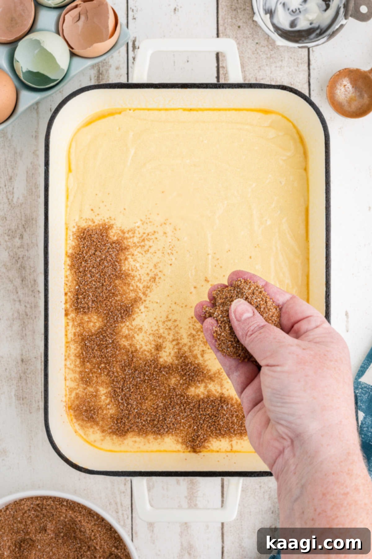 Half of the cinnamon sugar mixture being sprinkled evenly over the first layer of cake batter in the baking dish.
