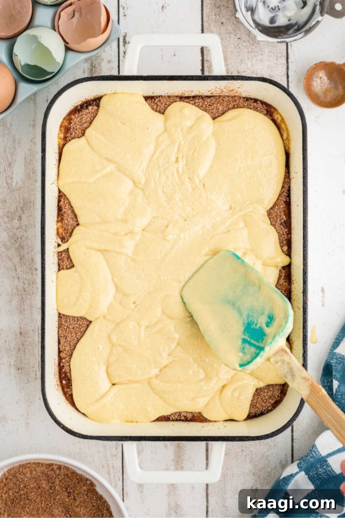 The remaining cake batter being carefully poured over the cinnamon sugar layer and spread to the edges.