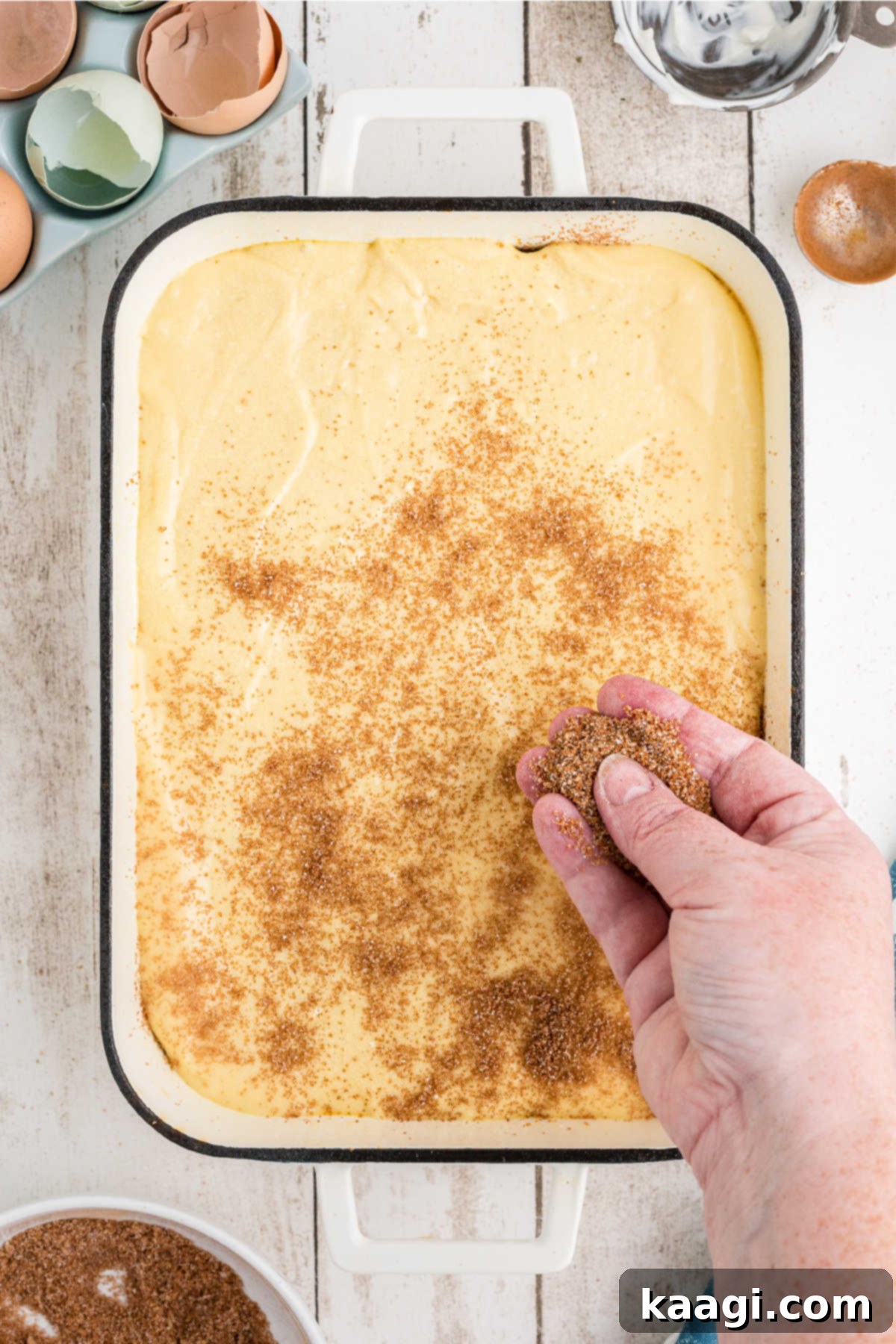 The remaining cinnamon sugar mixture being sprinkled evenly over the top layer of cake batter before baking.