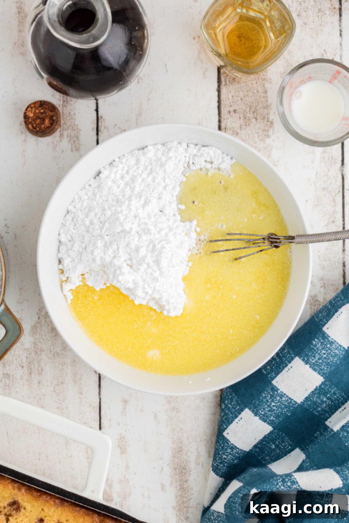 A small bowl with powdered sugar, melted butter, honey, vanilla, and milk being whisked together to form a smooth glaze.