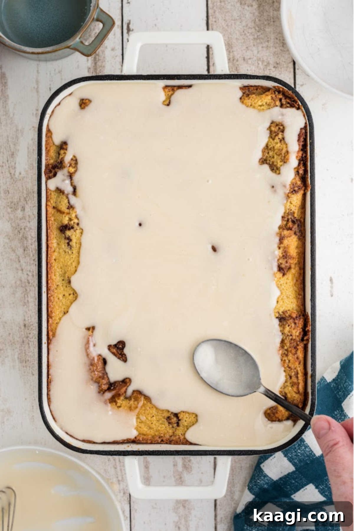 The prepared honey glaze being generously spooned and spread over the warm honey bun cake in the baking dish.