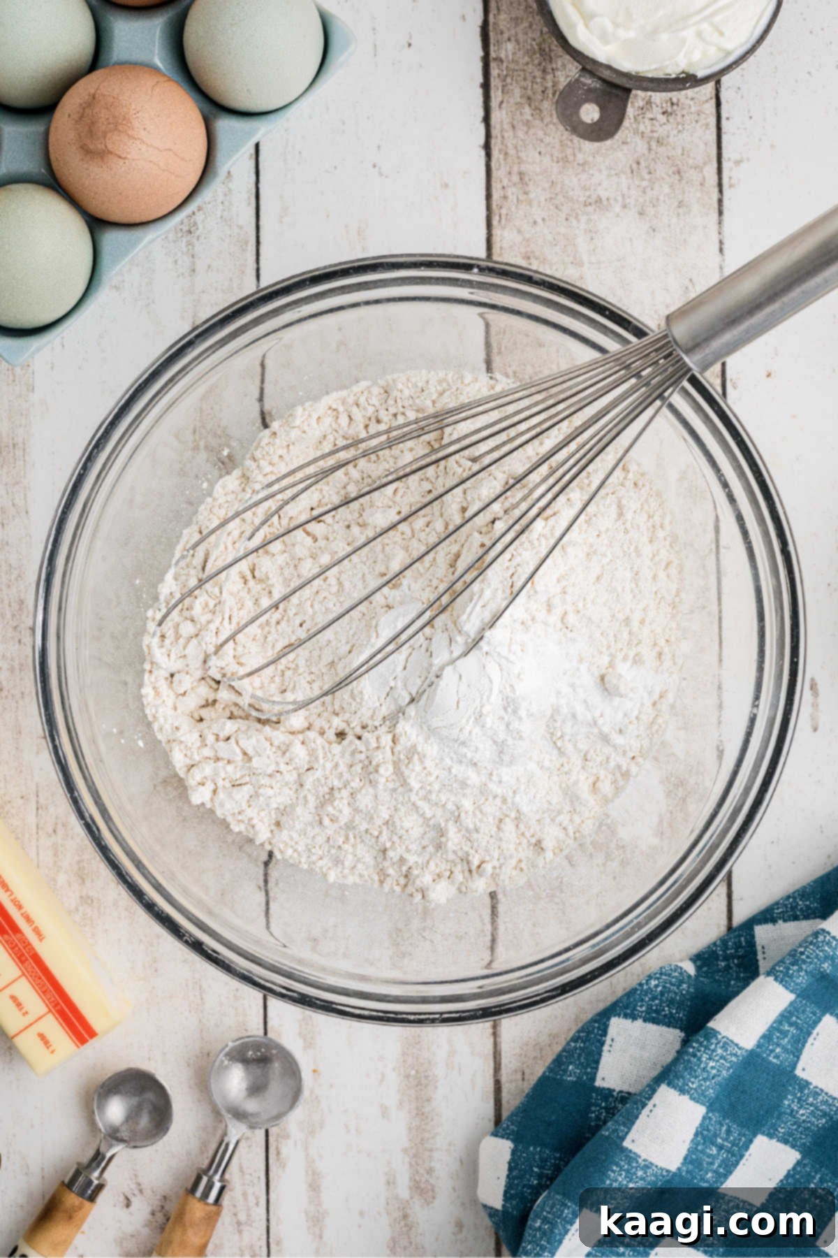 A medium mixing bowl containing flour, baking powder, baking soda, and salt, ready to be whisked.