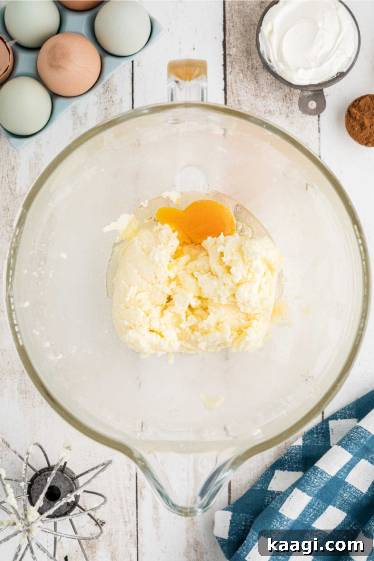 A single large egg being cracked and added to the creamed butter and sugar mixture in a stand mixer.