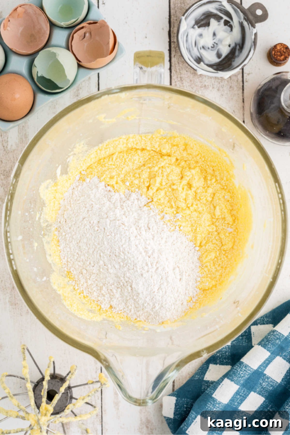 A scoop of the dry flour mixture being added to the wet cake batter in the stand mixer.