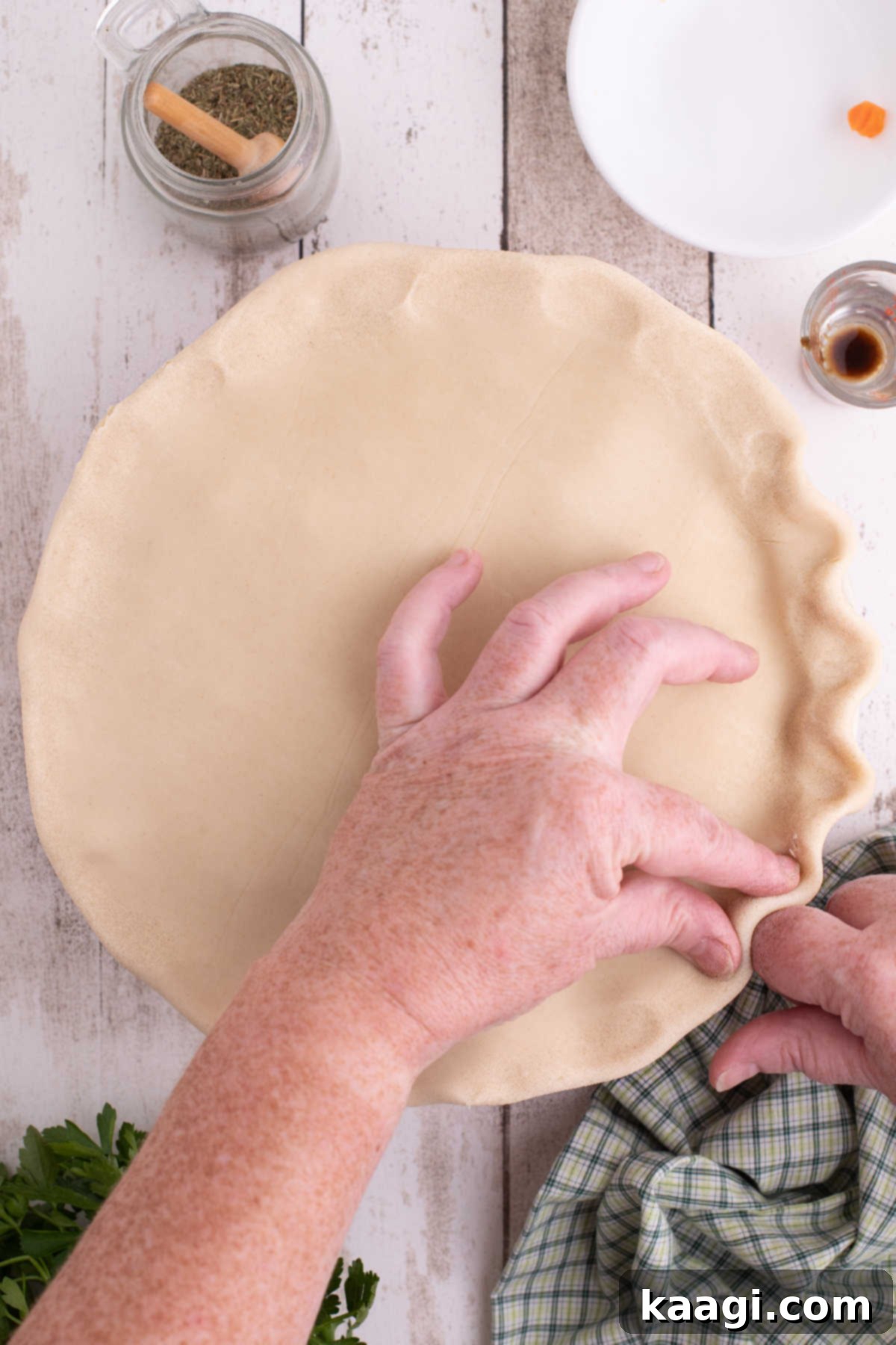 Pastry added to the top of a pie dish, being crimped around the edges by hand.
