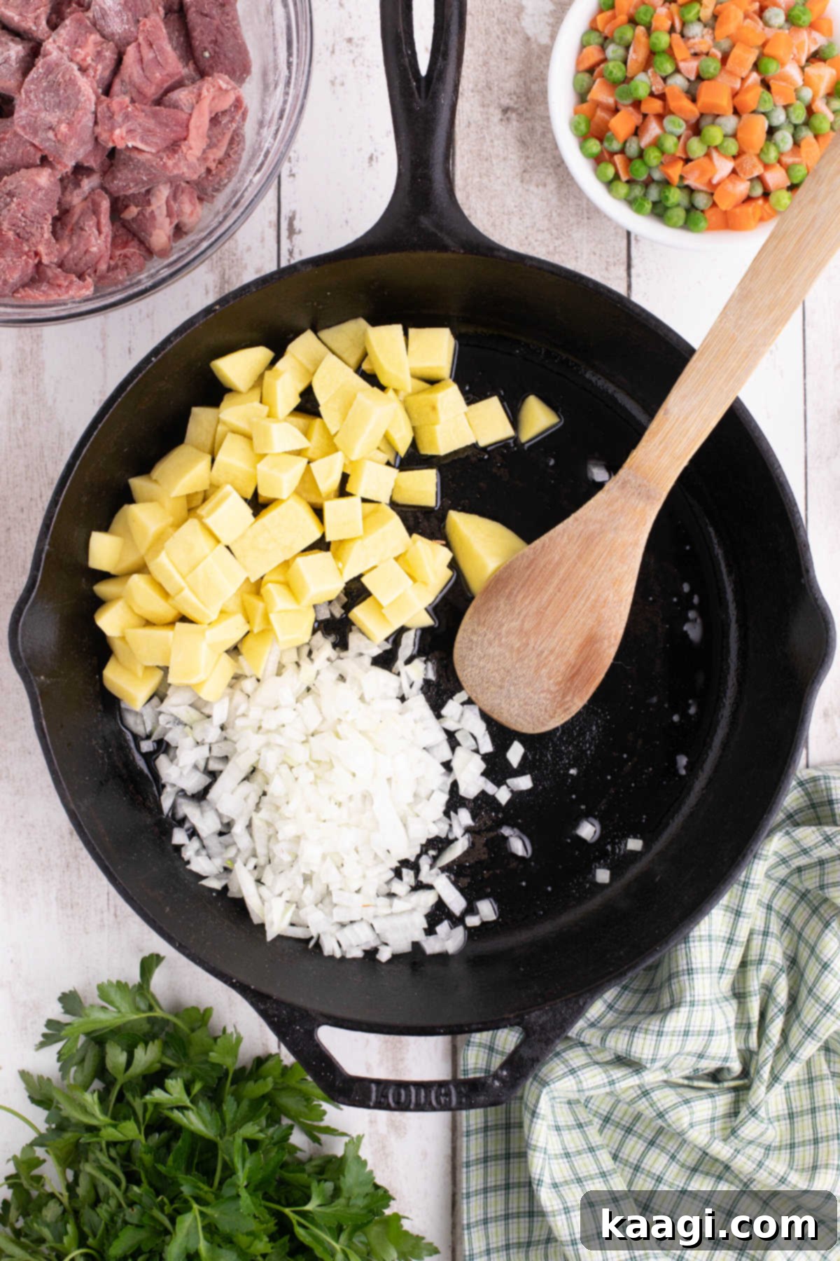 A large black skillet with oil, onions and potatoes in it.