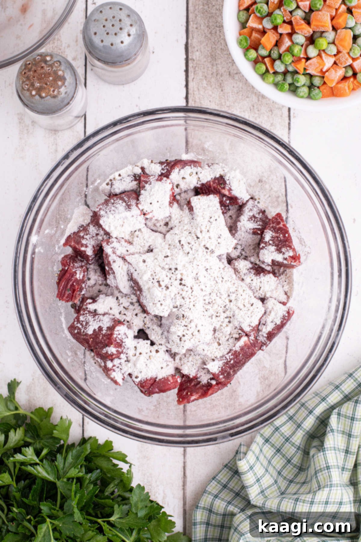 A large mixing bowl with cubed beef, flour and seasoning.