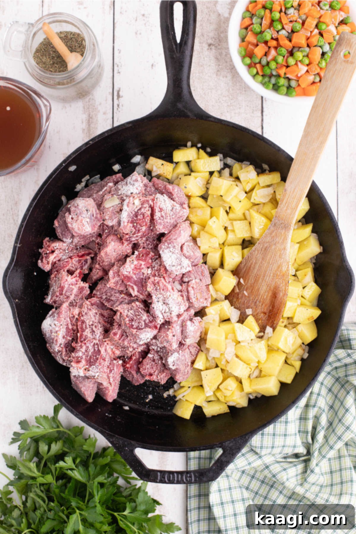 A large black cast iron skillet filled with seasoned beef, potatoes and onions.