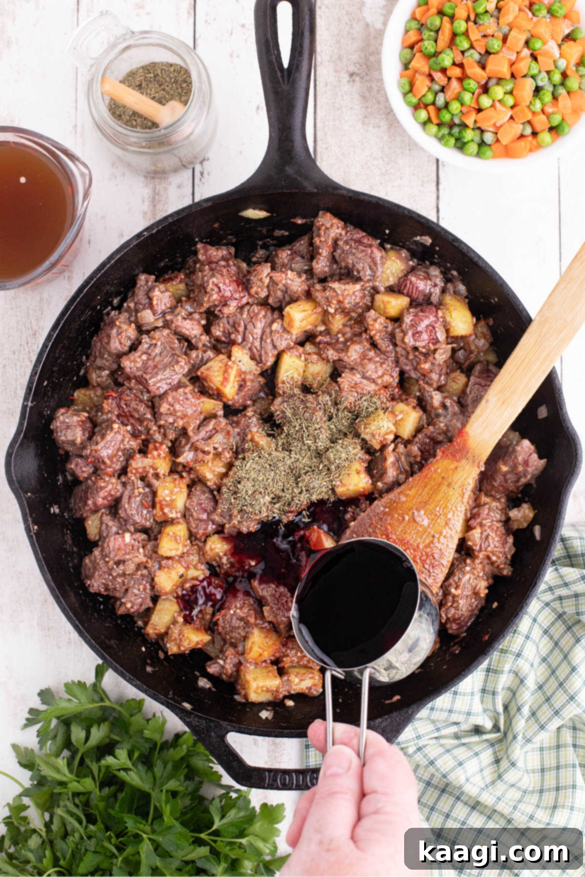 Beef and potatoes cooking in a large black skillet with red wine being poured in.
