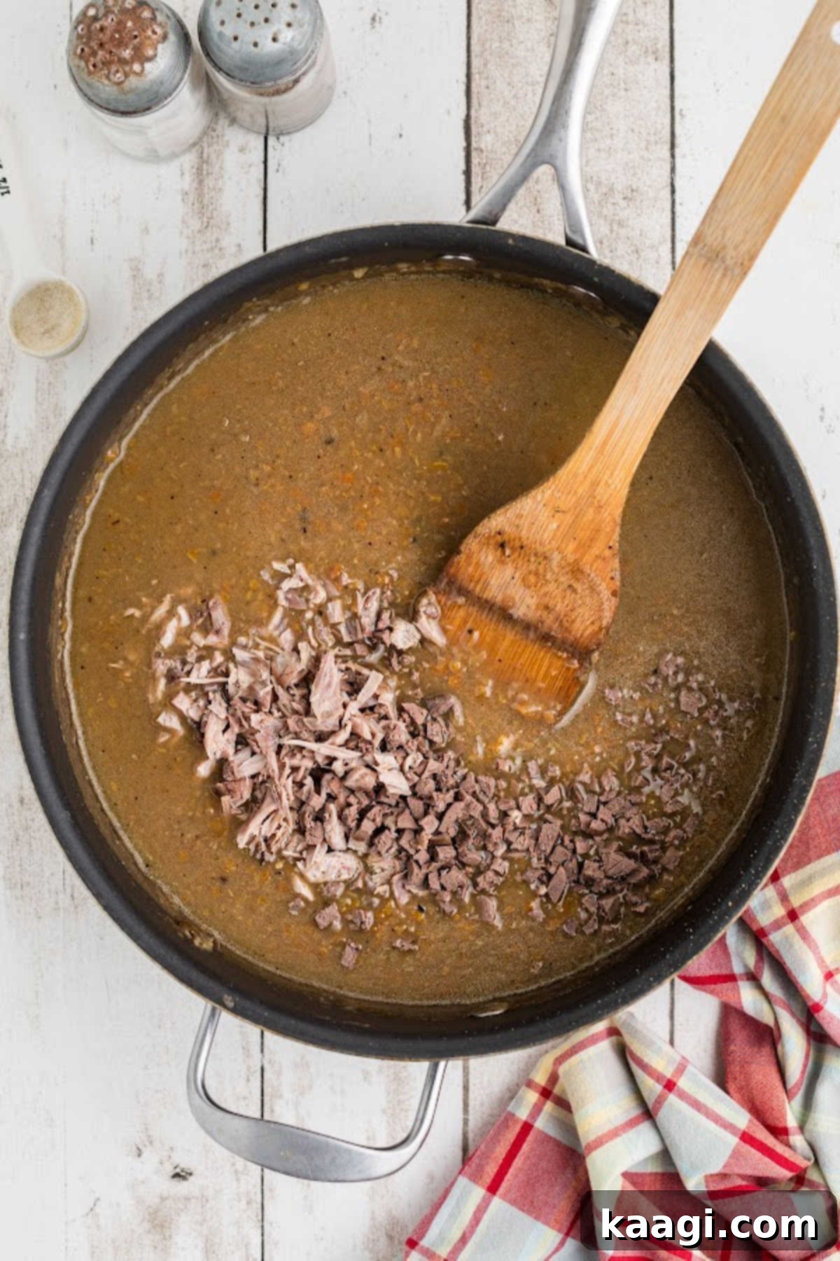 Meat added to a large skillet of giblet gravy, creating a rich and chunky texture.