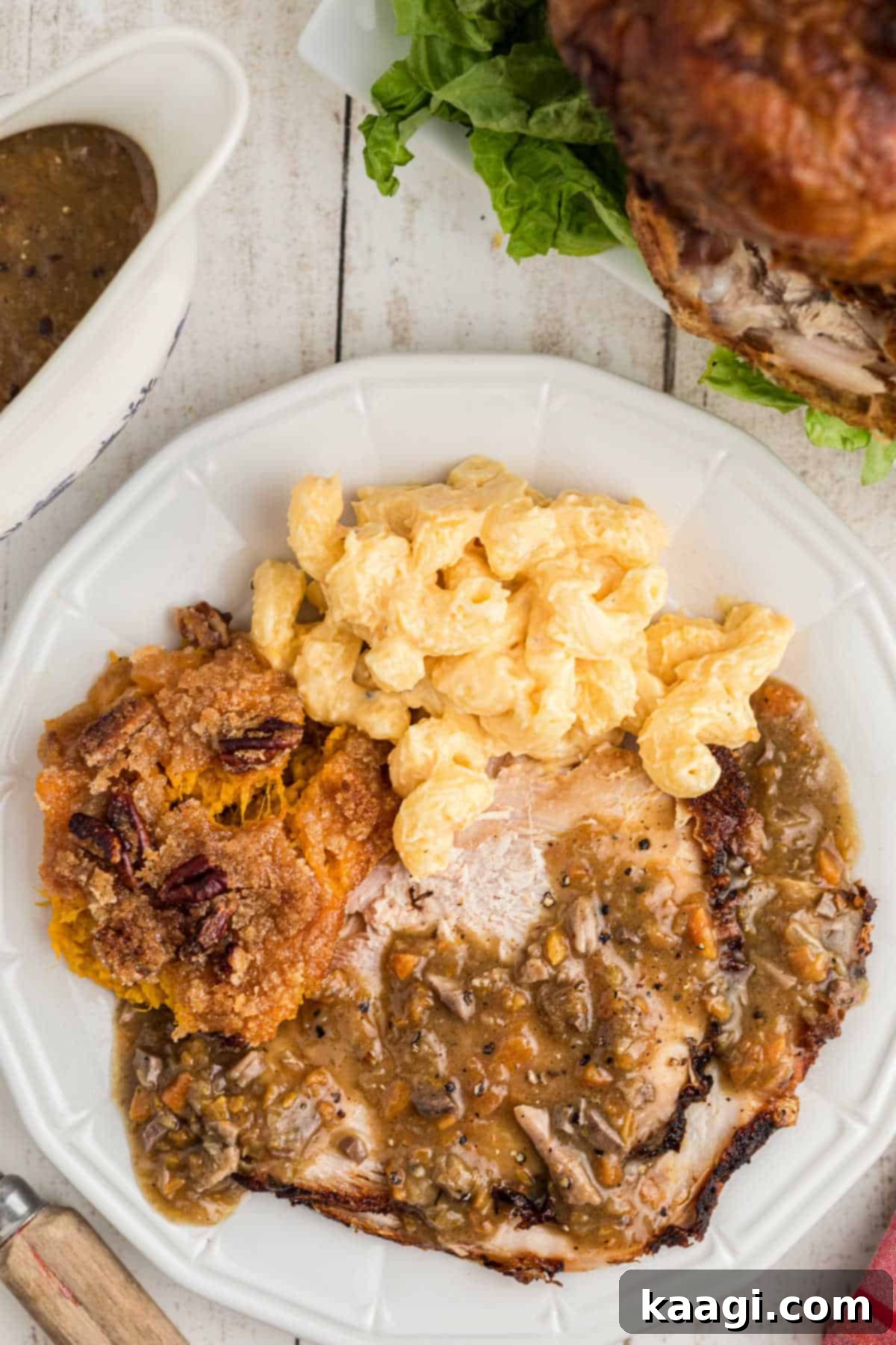 A delicious looking plate with turkey, mac and cheese and sweet potato casserole with giblet gravy poured over the turkey, showcasing a full holiday meal.
