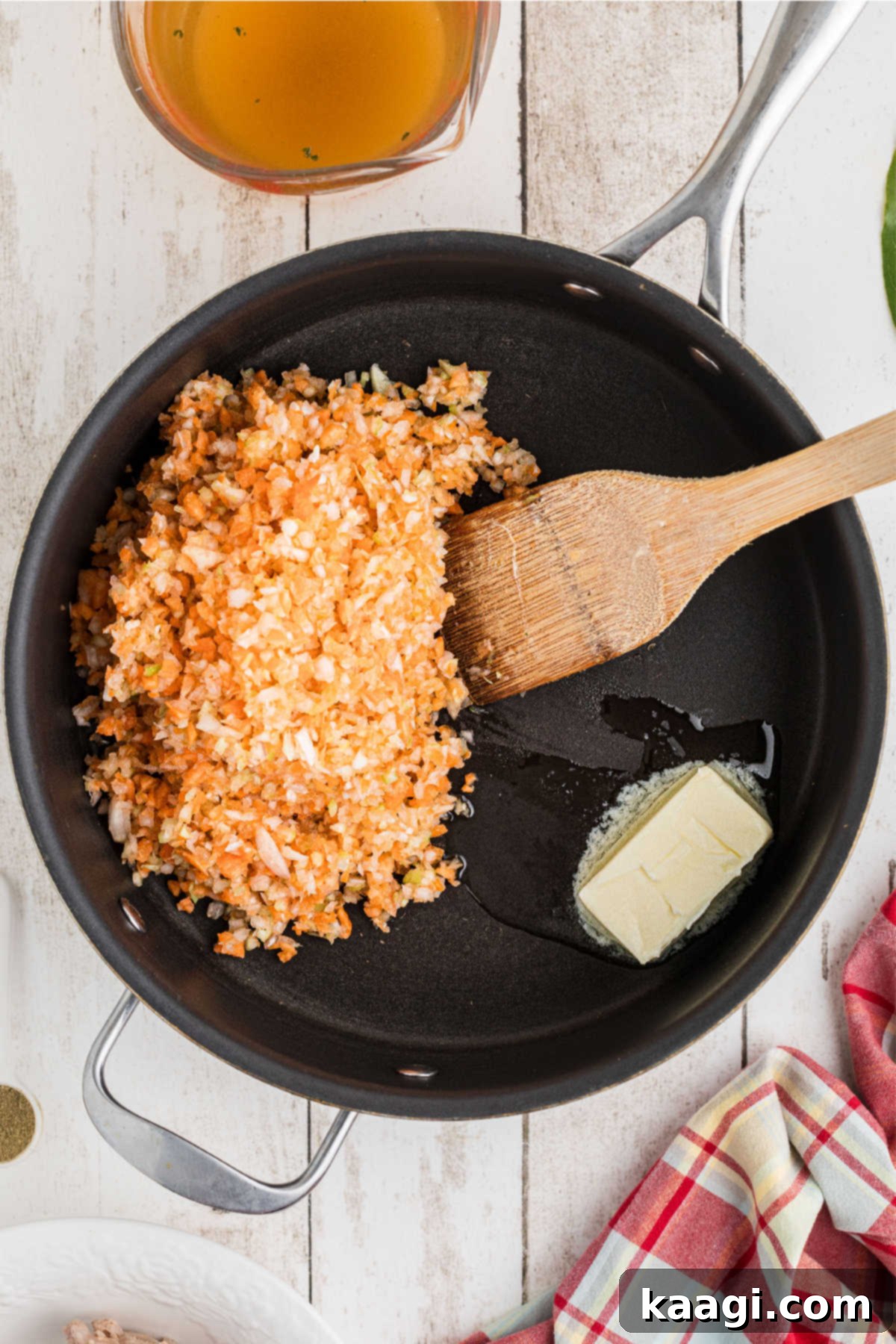 A large skillet with finely diced vegetables and butter, starting to soften and release their aromas.