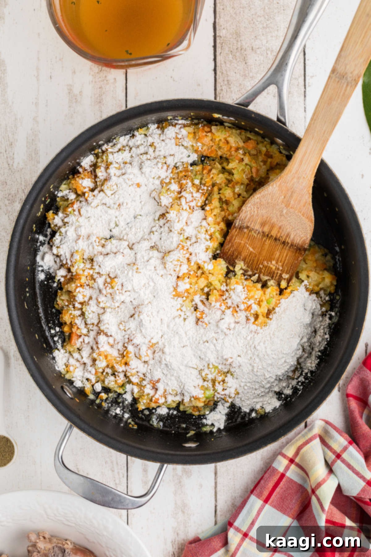 Flour added to a skillet of cooking vegetables, creating the start of a roux.