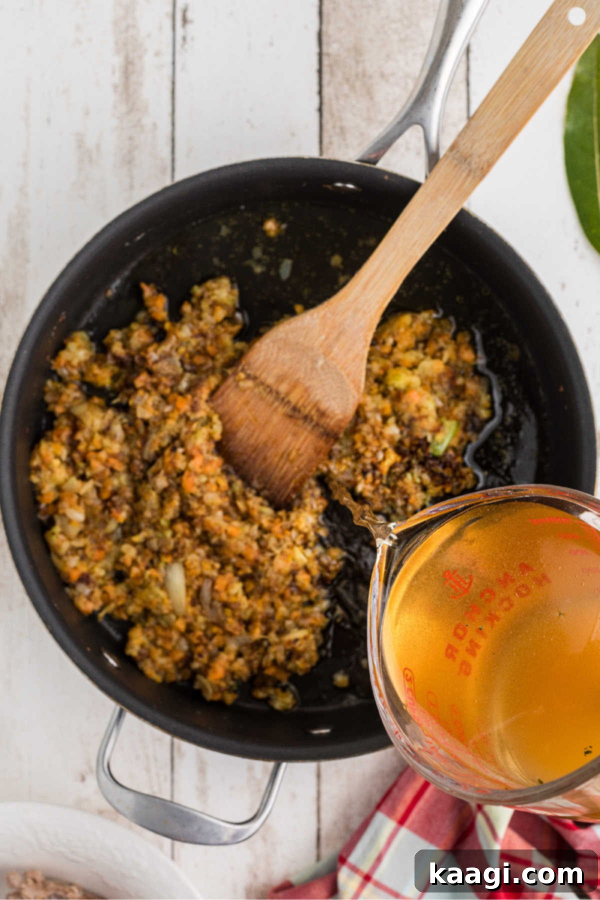 Slowly pouring chicken broth into a large skillet of cooking vegetables and roux, whisking constantly to ensure smoothness.