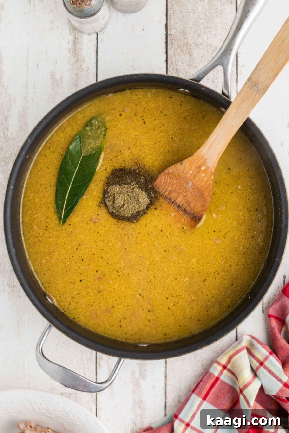 Seasonings added to a skillet of gravy with a bay leaf, simmering to deepen flavors.