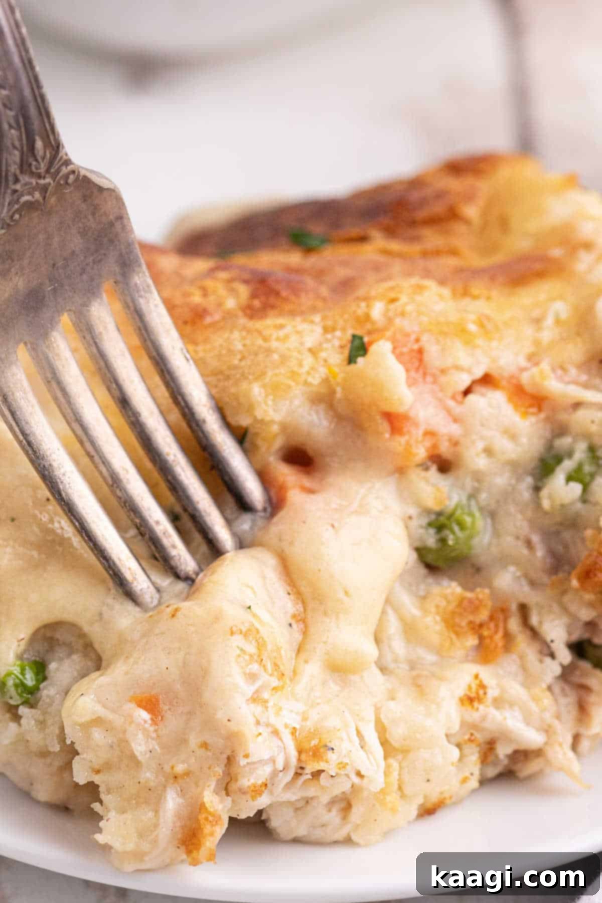 Close up portrait image of a chicken cobbler recipe with a fork digging into it, showcasing the golden biscuit topping and creamy filling.