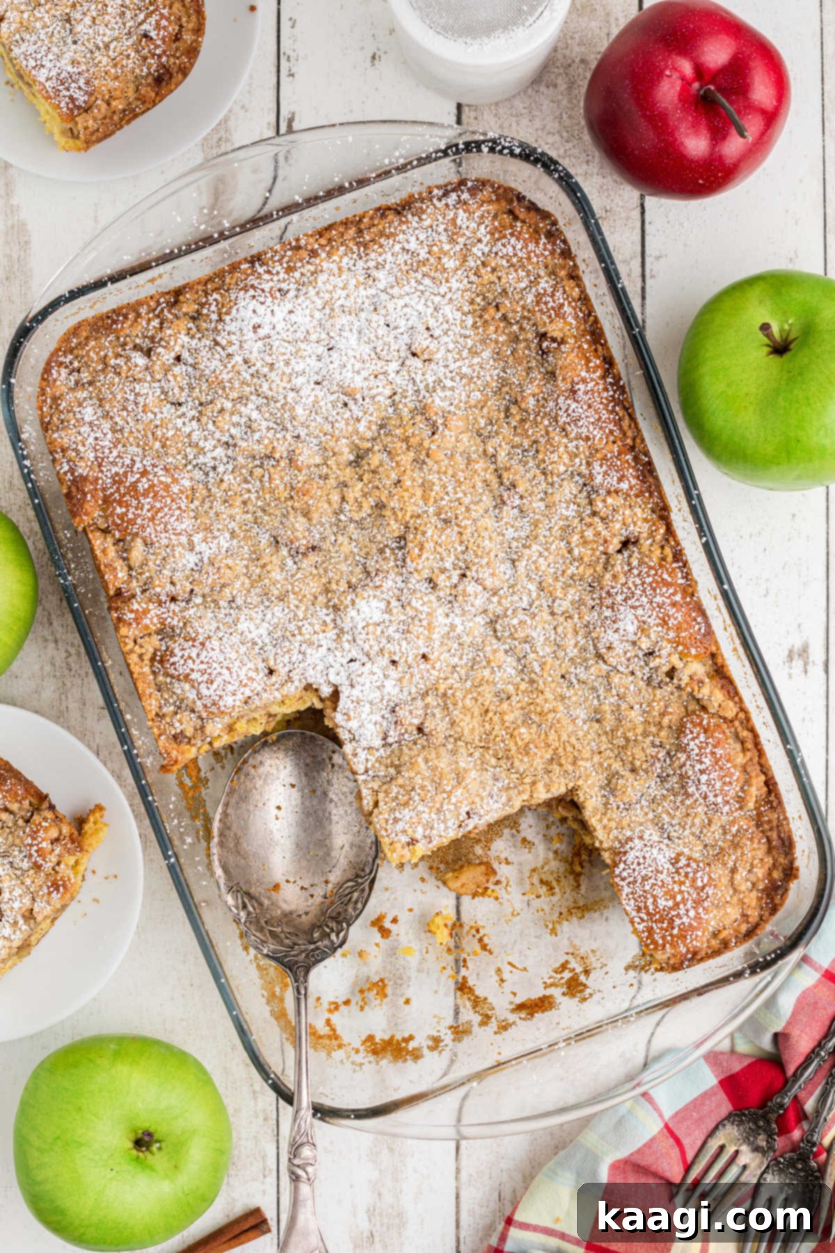 An overhead shot of a freshly baked apple pie cake in a 13x9 inch baking pan, with several slices already removed, showing the golden crumb topping and rich apple filling.