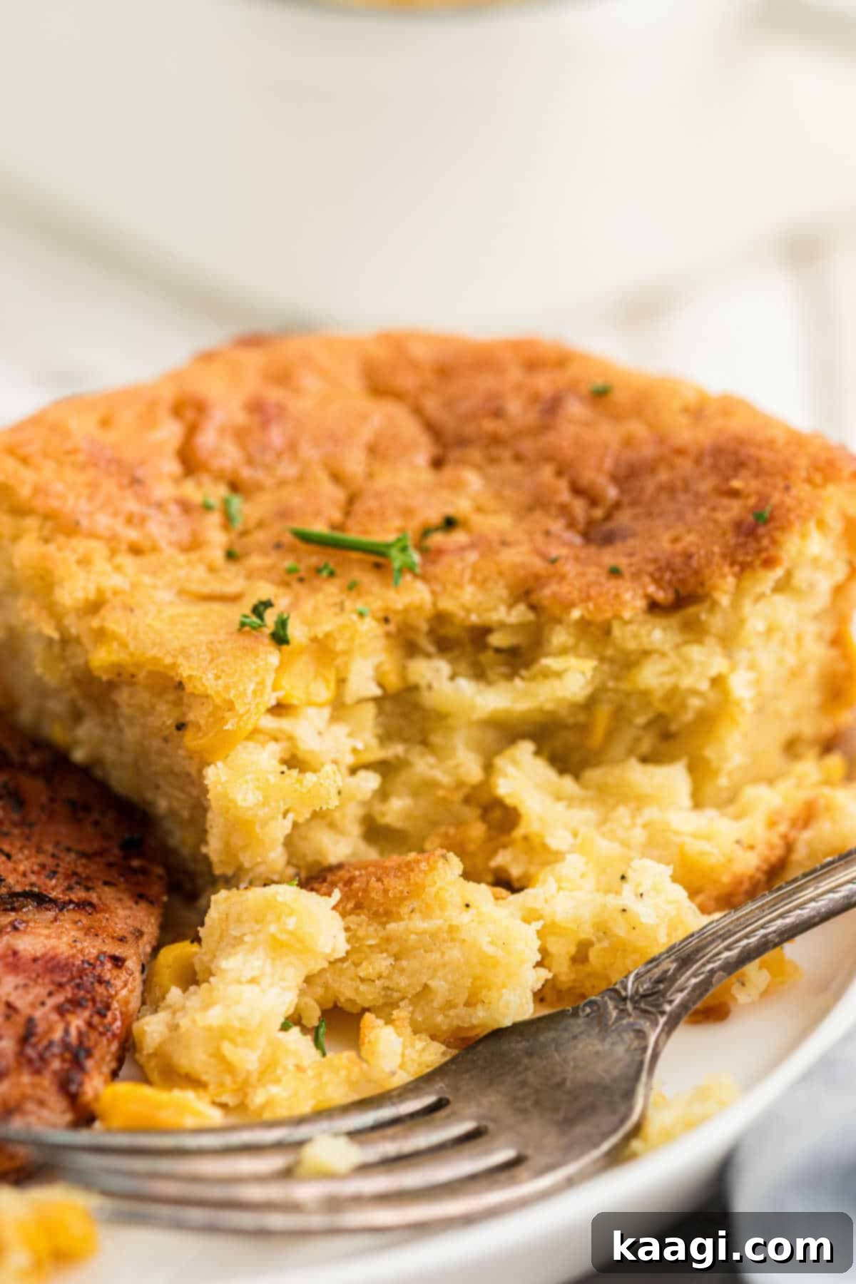 Close up of a dished up serving of cornbread pudding with a fork resting next to it, ready to be enjoyed.