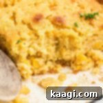 Close up shot of a dish of cornbread pudding with a wooden spoon resting.