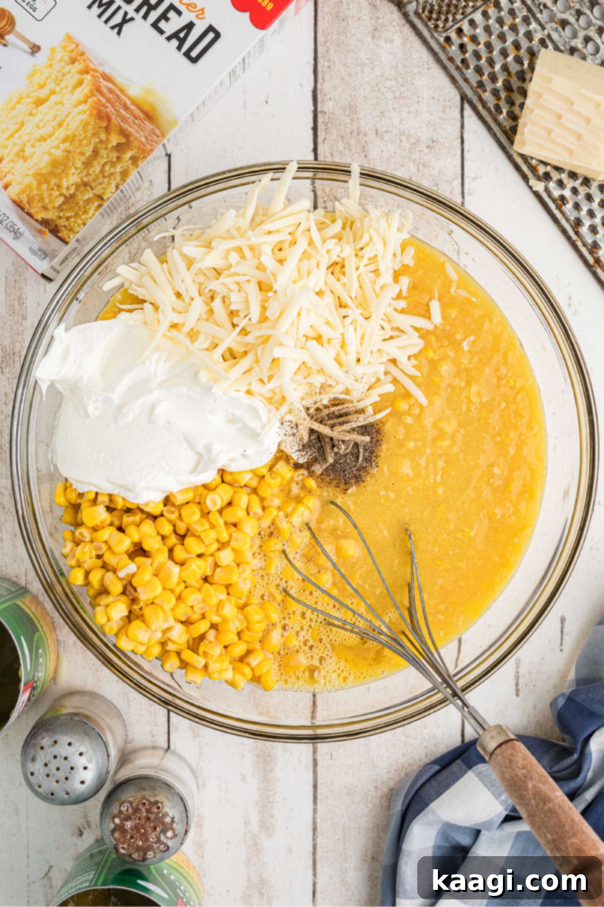 A mixing bowl filled with corn kernels, cream-style corn, rich sour cream, and grated cheese, ready for mixing.