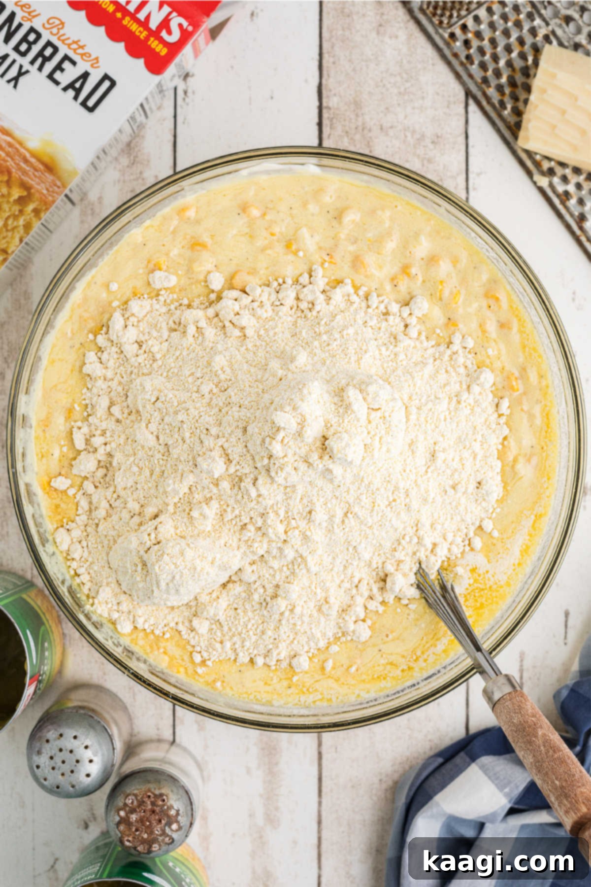 Cornbread mix being gently folded into a mixing bowl containing other pudding ingredients.