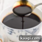 A bowl full of browning sauce, with a spoon lifting some out, showing its deep, glossy texture.