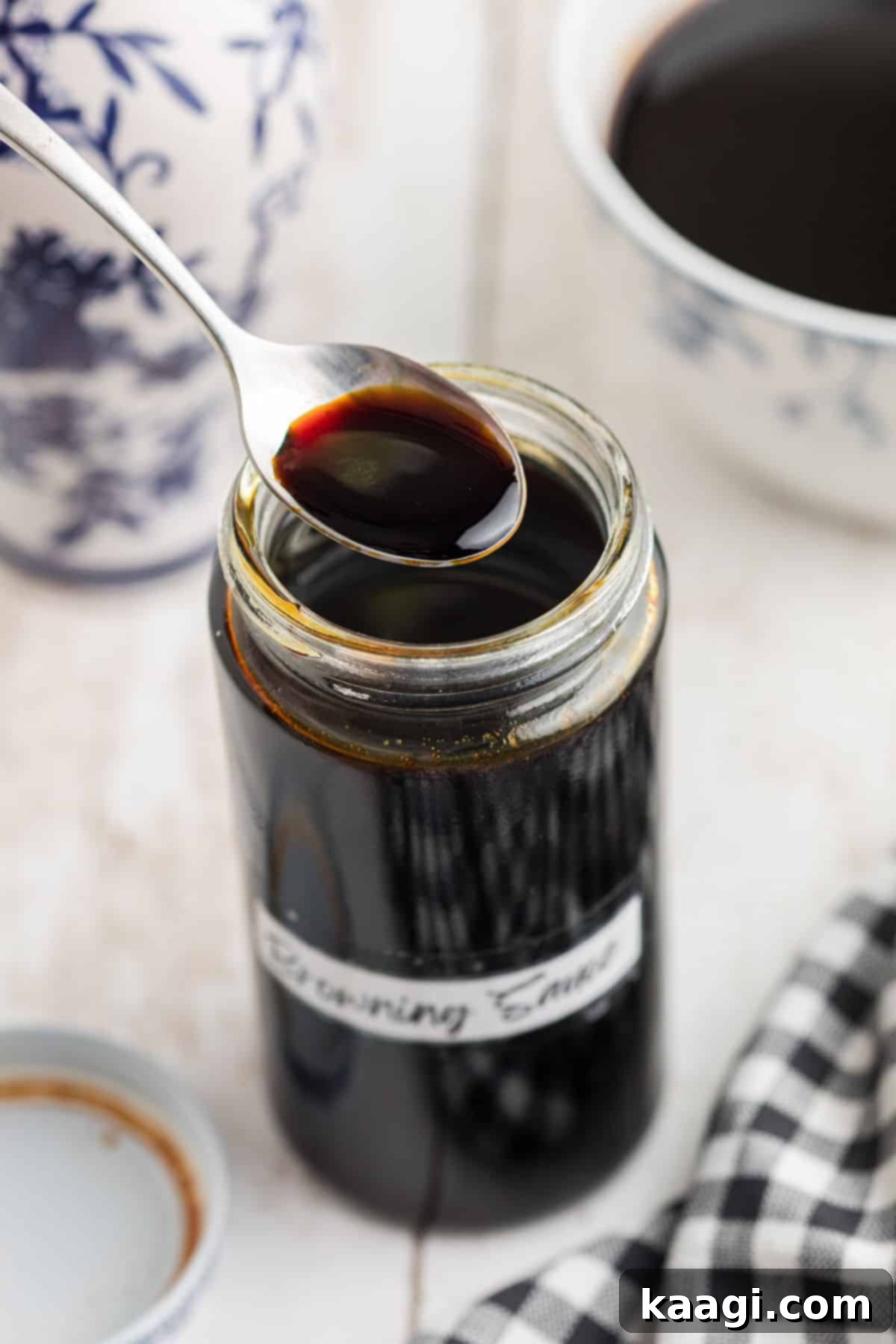 A jar of browning sauce with a homemade label, with a spoon lifting some out, showing its deep, glossy texture.