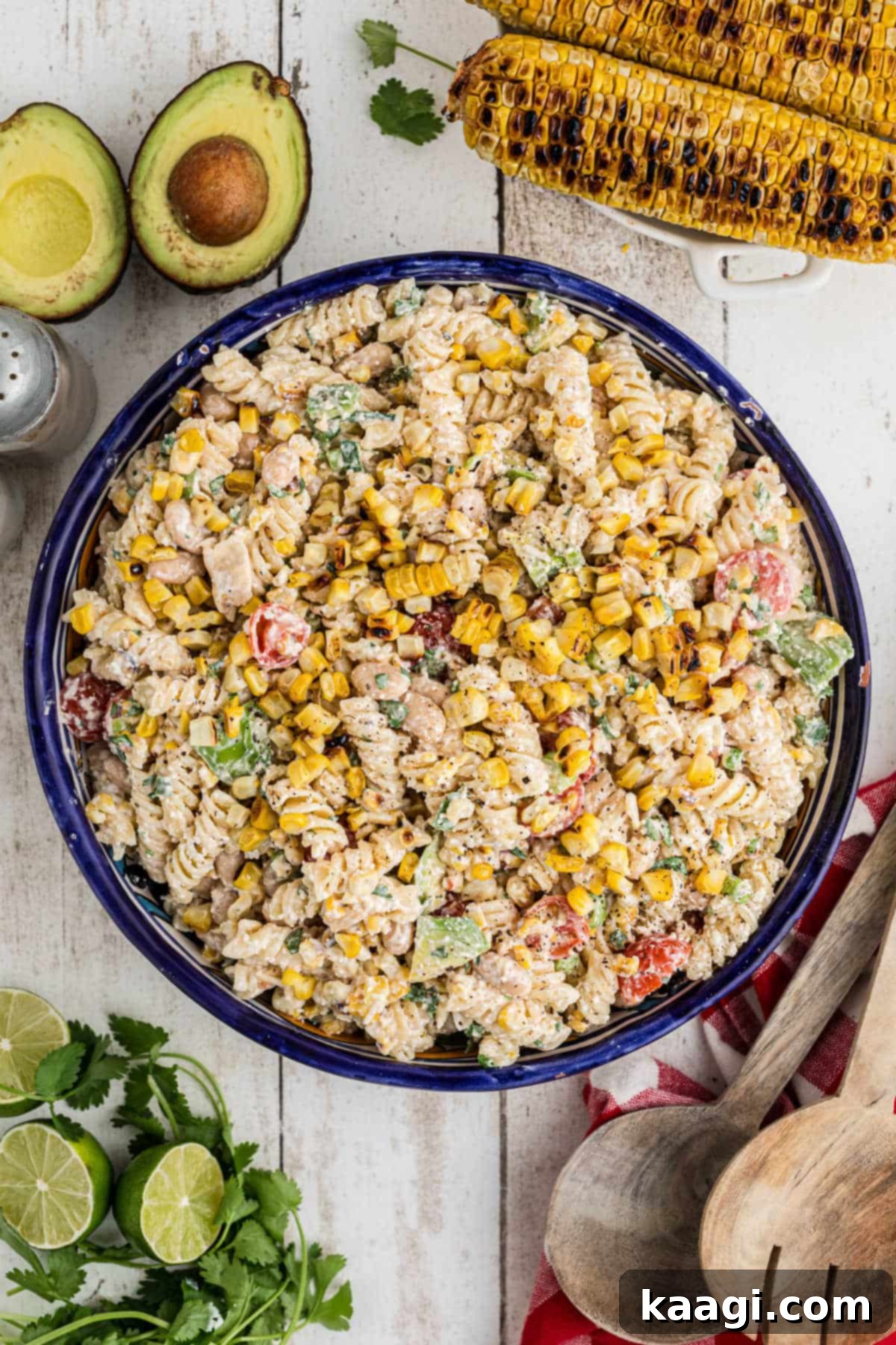 Overhead shot of a bowl of Elotes pasta salad with some grilled corn cobs in the background, ready to serve.