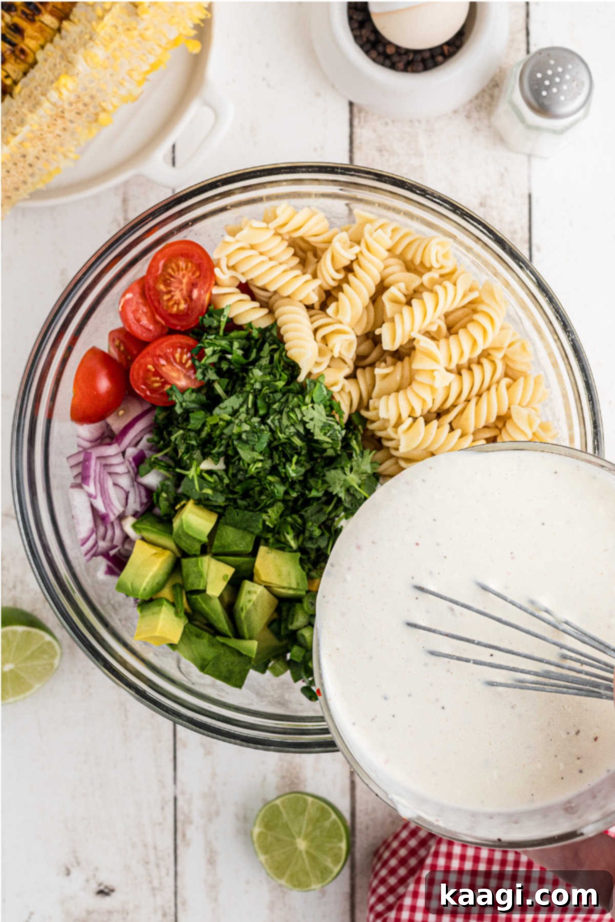 The creamy cilantro lime dressing being poured generously over the bowl of pasta and salad ingredients, ready for a final toss.