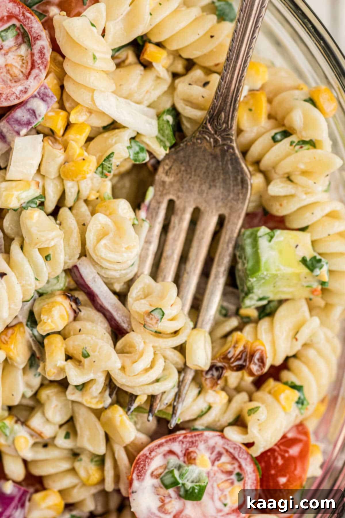 A very close-up view of a bowl of cilantro lime pasta salad, with a fork gently scooping into the creamy, colorful mixture.