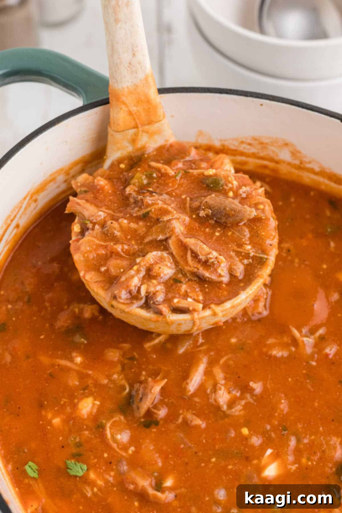 Close-up of a ladle scooping out rich, dark Louisiana turtle soup from a large pot, garnished with fresh herbs.